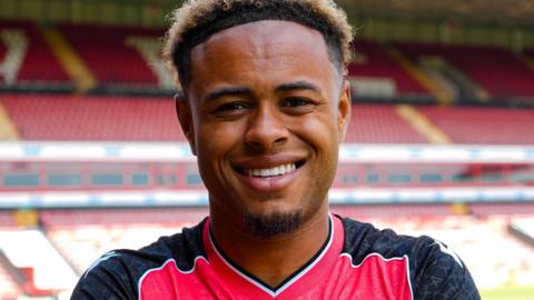 Head shot of new Walsall signing Tai Sodje in a home shirt. The empty stands of the Pallet-Track Stadium are behind him.