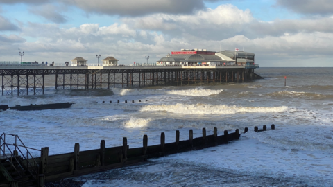 Cromer Pier, as seen from near the beach. In the foreground is water, which looks choppy, and in the background is the pier. The Pavilion Theatre is at the end of the structure.