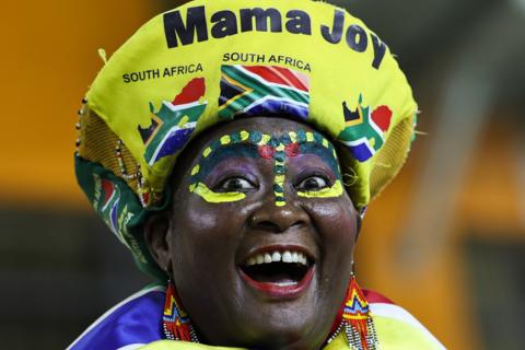 Close-up headshot of Sout African superfan Mama Joy, wearing a hat with her name on it and a South African flag, pulls a funny face looking into the camera