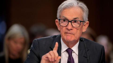 The chair of the US Federal Reserve, Jerome Powell, wearing a suit and tie testifying before the US Senate banking committee. He is raising his finger.