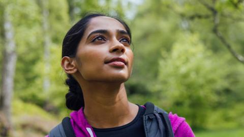 A young woman looks up into trees.