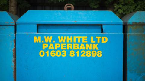 A blue paper bank with yellow writing which says M.W. WHITE LTD PAPER BANK with a phone number of the company. 