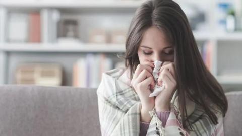 A woman blowing her nose while wrapped in a blanket.