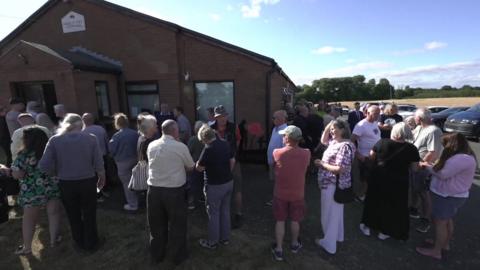 A crowd of people outside a community hall