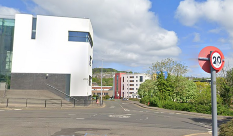 A mini roundabout with a 20 mph traffic sign and a white building in the foreground 