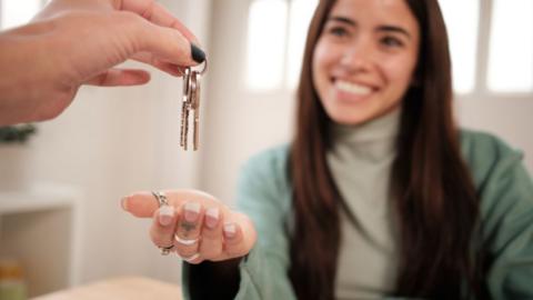 A smiling woman holds her palm out under a set of keys held by someone else out of shot.