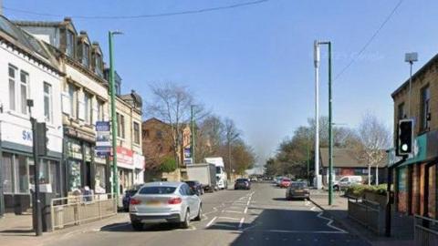 A street in Bradford. It is busy with cars, with shops and restaurants on both sides of the street. 