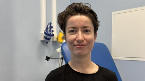 Dr Aoife Fordham, an urgent treatment centre doctor in a NHS clinical room wearing a black T shirt.