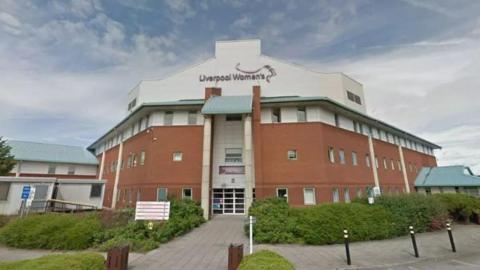 An exterior shot of Liverpool Women's Hospital , the white and brick building stands behind the entrance, with the sign saying Liverpool Women's 