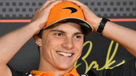A smiling Oscar Piastri with his hands on his McLaren cap during a news conference before the Azerbaijan Grand Prix