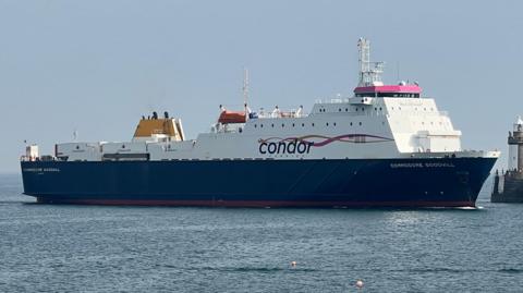 A large commercial vessel, the Commodore Goodwill, heading into a harbour. Skies are blue.
