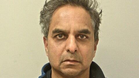 Police mugshot of Dr Amal Bose. He has short, unkempt dark hair that is greying and is looking directly at the camera, frowning slightly. He has brown eyes and bushy eyebrows.
