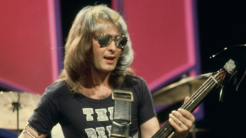 Pete Overend Watts of Mott the Hoople on Top of the Pops in 1974. He has long brown hair with sunglasses on while he plays the guitar. 