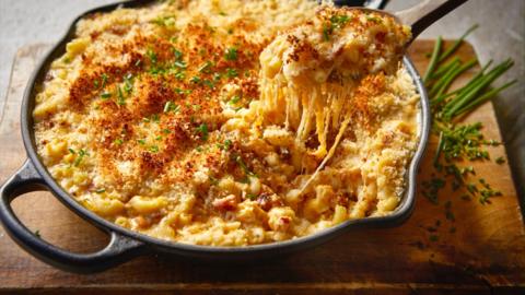 Top down view of a dish with handles full of macaroni cheese. A large spoon is removing some from the dish 