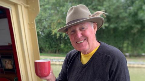 Man with grey hair holding cup of tea on his boat in Foxton Locks