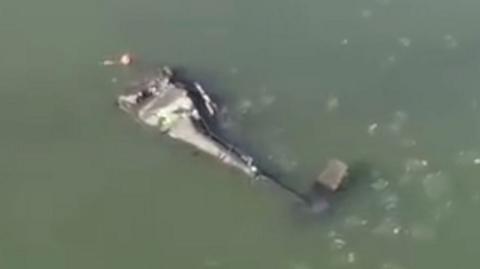 A crashed Army helicopter lies on its side in the Potomac river.