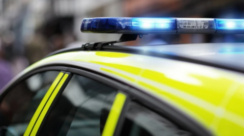 A close-up photo of a yellow police car with a blue light on the top