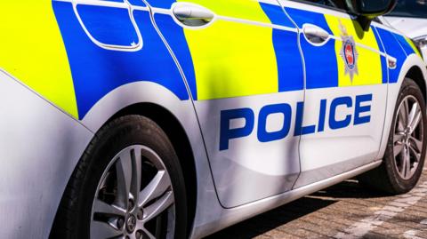 An up-close shot of a police car. It is yellow and blue. 