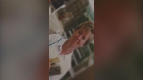Blurred and old photo of a woman wearing a white shirt and holding a newspaper. She has dark blonde hair.