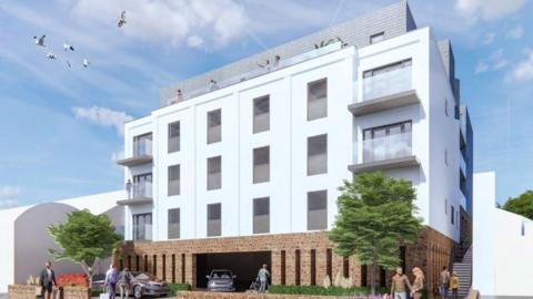 A CGI mock up of the building plans. The image shows a large white building with windows and balconys. A stone wall runs around the building. Trees are growing in front of it and cars are parked. 