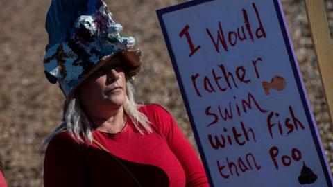 Campaigner against dumping sewage into the coast around Kent, stands with a sign which reads I would rather swim with fish than poo. 