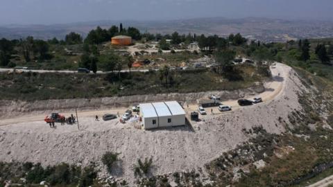 An aerial view shows people around a portable building under construction at the illegal Israeli settler outpost of Homesh, near the Palestinian village of Burqa, in the occupied West Bank (29 May 2023)
