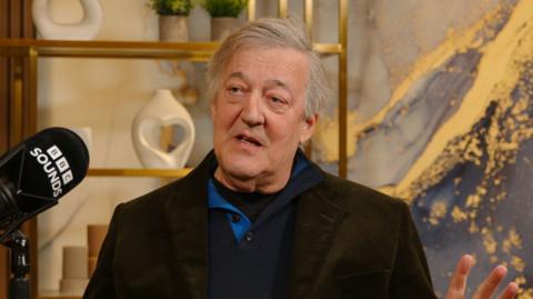 Stephen Fry wear a black jacket 