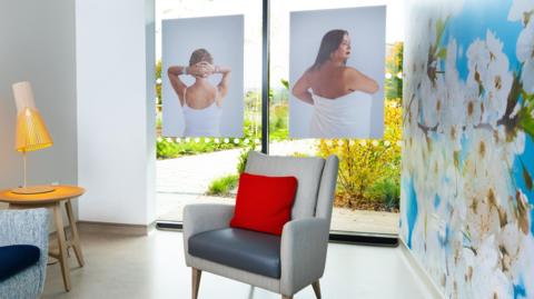 A care centre waiting room with two large pictures of women in white, one in a vest top, another in a towel. The waiting room is colourful with a large decal of cherry blossom on the wall.