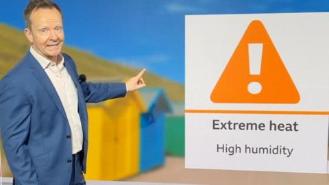 Man in blue suit and white shirt points at an 'Extreme heat' warning.