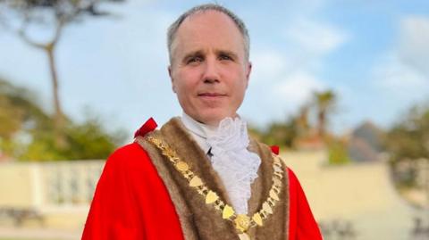 Mayor in chain and robes in front of blue sky and tree