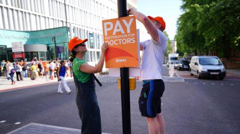 Two doctors pinning a sign to a pole