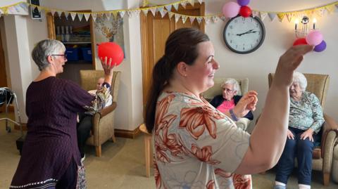 Susan Schibli and Krizsti Boros play a balloon catching game with care home residents in the lounge at Milward House