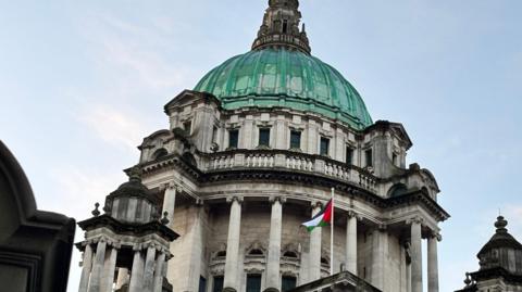 Palestine flag flying at Belfast City Hall. The sky is blue with white clouds.