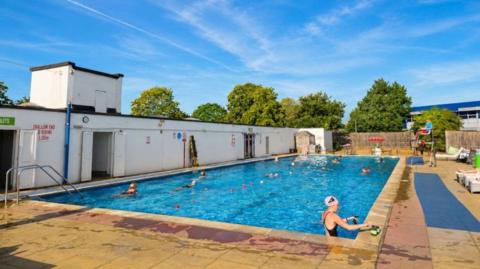 An outdoor swimming pool with swimmers on a sunny day.