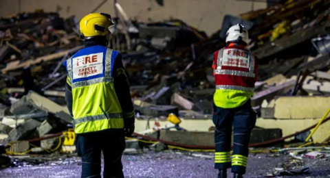 Two firefighters in hi vis look at a large pile of debris.
