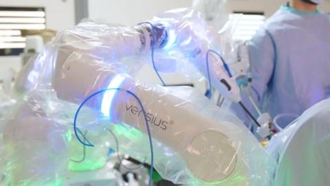 A white robotic arm with two sections lit with blue light is covered in protective clear plastic.