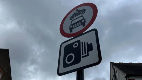 Circular red sign with car and bike inside and square camera sign just below
