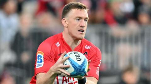 Dallas McLeod holds the ball in two hands in front of him while on the pitch during a match for Crusaders