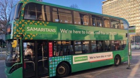 A photo of the green bus parked in Plymouth city centre. It is green and has the charity's logo on the side of it.