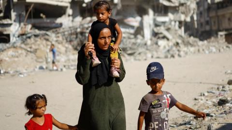 Palestinians walk past ruined buildings as they return to Khan Younis 