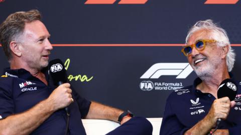 Christian Horner and Flavio Briatore speaking into FIA-branded microphones at a Formula 1 news conference