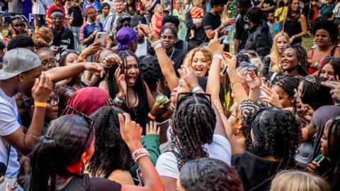 A big group of happy festival goers with arms in the air dancing to music.