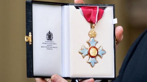 CBE award in its presentation case, being held in someone's hands