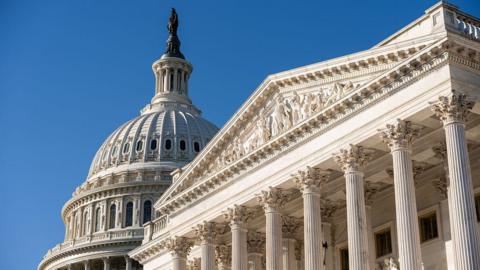 A view of the outside of the US Capitol building in Washington DC against a bright blue sky.