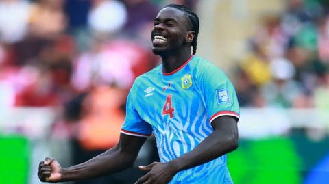 DR Congo defender Axel Tuanzebe celebrates a goal for his country against Jamaica in their World Cup play-off win. He is seen from waist up clenching his right fist at waist level while tilting his head up slightly, with eyes closed and a look of delight on his face