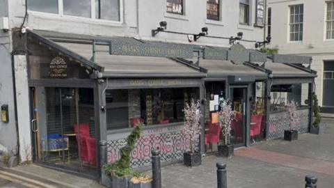Streetview of the Wafi Lounge, it is a grey building with a glass conservatory-style section wrapping around the building.