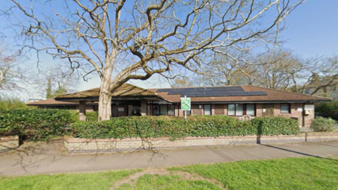 A buildings with a row of bushes in front of it. A tree also stands in front of it.