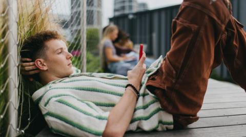 A young man lying down on the ground holding and scrolling on his smartphone.