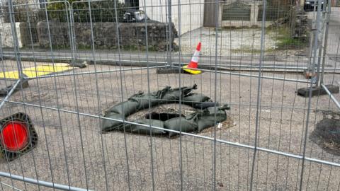 A picture of the mineshaft hole. There is a silver fence surrounding it.