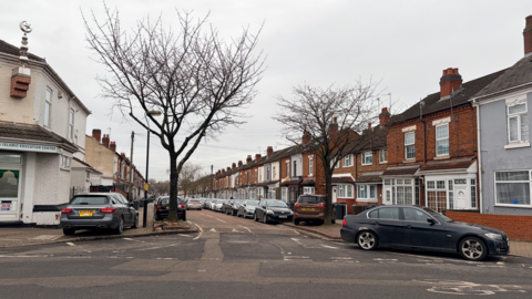 Cars parked on the side of the road and on the pavement on a residential street.